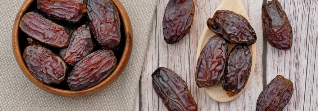 Eine Schale mit Datteln und einige Datteln auf einem Holzbrett, gesundes Snackprodukt.