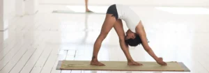 Eine Person in einer Yoga-Pose auf einer Matte, die sich nach vorne beugt und eine Hand auf den Boden legt.